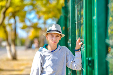An angry and displeased guy in a hat holds on to a green fence and looks at the camera.の写真素材
