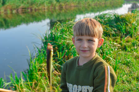 Joyful and surprised boy holds a fish hanging on a fishing rod.の写真素材