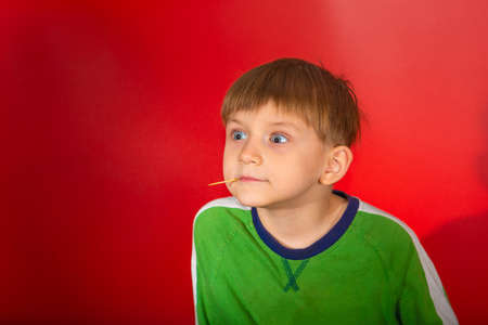 Astonished boy looks away with a toothpick in his mouth on a red background.の写真素材