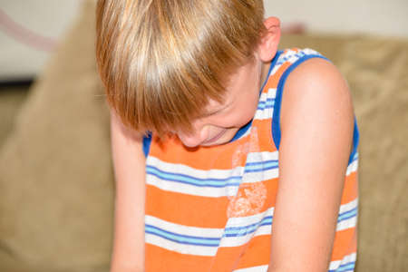 The boy sits and cries on the couch with tears after punishment.の写真素材