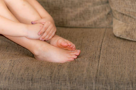 Hands of a man lying on his feet, sitting on a sofa.の写真素材
