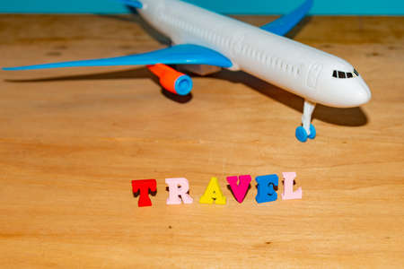 Tourism and travel concept, toy airplane and color letters on wooden background.