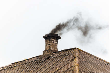 Black smoke from the chimney of an apartment building during heating and heating on the roof of slate.の写真素材