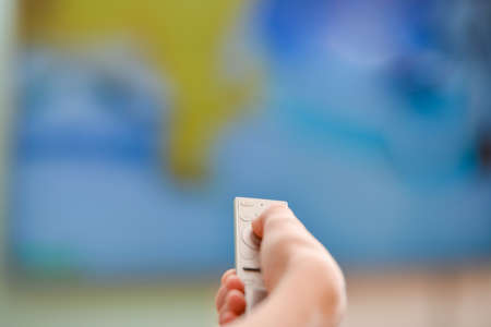 A man's hand holds a TV remote control to switch channels.の写真素材