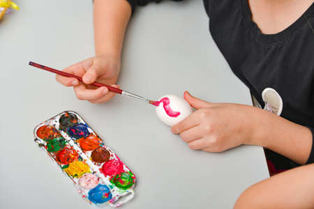 Children paint eggs for Easter, paints draw patterns on a white egg.の写真素材