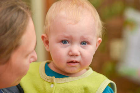 A small child sits in her mother's arms and cries with tears in her eyes.の写真素材