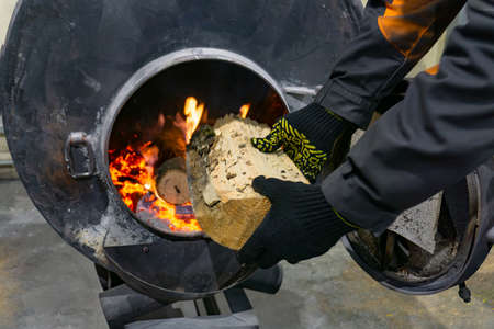 A worker throws firewood into an oven to heat a room.の写真素材
