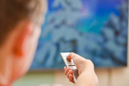 A man watches TV and directs the remote control to the screen.の写真素材