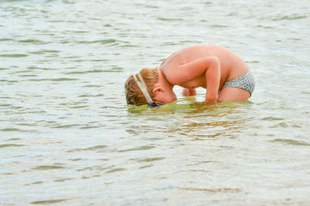 A boy with glasses for diving stands on the seashore.の写真素材