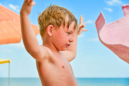 A boy at the sea on the beach among sun umbrellas spread his hands to the sides.の写真素材