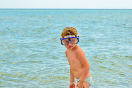 A boy with glasses for diving stands on the seashore.の写真素材
