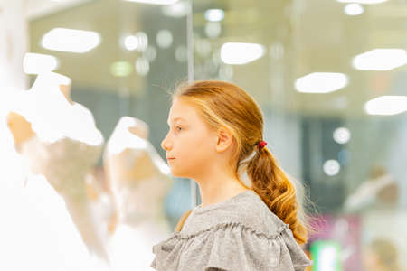 A young girl, a teenager, stands near the window of a wedding salon and looks at wedding dresses, introducing family life.の写真素材