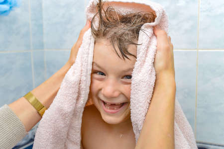 Mom wipes the baby with a towel after bathing in the shower, a joyful and happy boy in the bathroom.