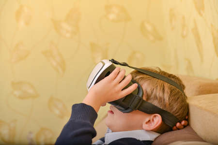 A boy in a virtual reality helmet watches a video at home on the couch.
