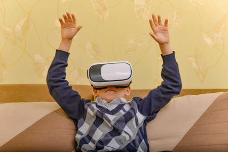 A boy in a virtual reality helmet watches a video at home on the couch.