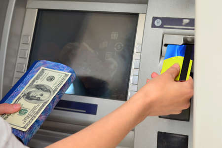 A woman inserts a plastic card into an ATM to withdraw cashの写真素材