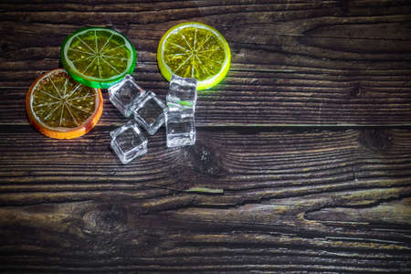Ice cubes and slices of multi-colored lemon on a dark wooden background. Copy spaceの写真素材