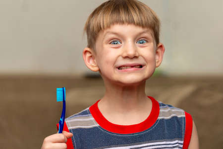 The boy holds a toothbrush in his hand showing clean teethの写真素材