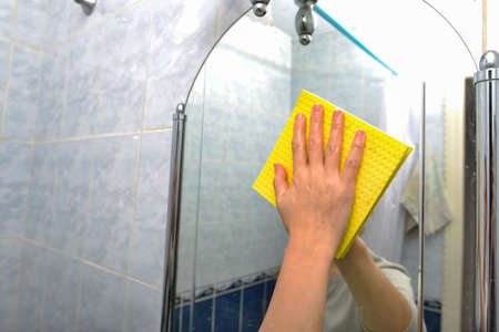 A woman cleans the bathroom, wipes the mirror with a yellow ragの写真素材