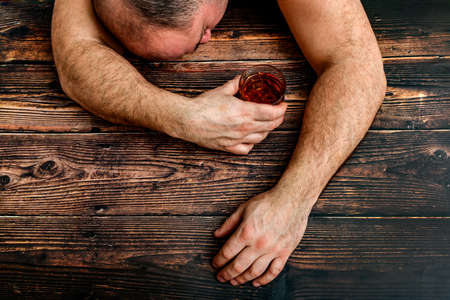Drunk man with a glass of alcohol lies on a wooden table. The concept of alcoholism and alcohol...