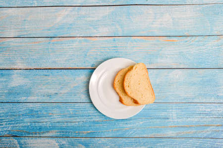 Slices of sliced white bread lie on a white plate, on a white wooden background