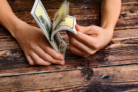 Man leafing over a bundle with dollars on a dark wooden background, concept of financial...