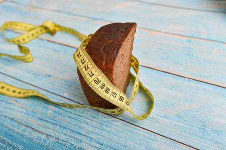 Brown bread wrapped in yellow centimeter on a blue wooden background, concept of slimming and healthy eatingの写真素材