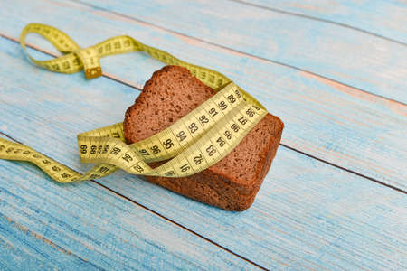 Brown bread wrapped in yellow centimeter on a blue wooden background, concept of slimming and...