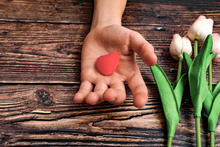 Man offers a heart and tulips on a brown wooden background. The concept of the holiday of Valentine's Day, and International Women's Day March 8の写真素材
