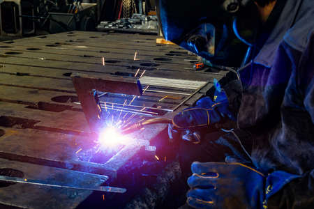 A welder in a workshop joins parts with a weld, sparks and smoke from weldingの写真素材