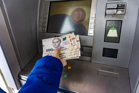 A woman at an ATM holds 500 hryvnia notes in her handの写真素材