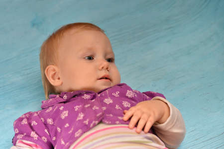 Little child on a blue wooden, joyful girl looks around