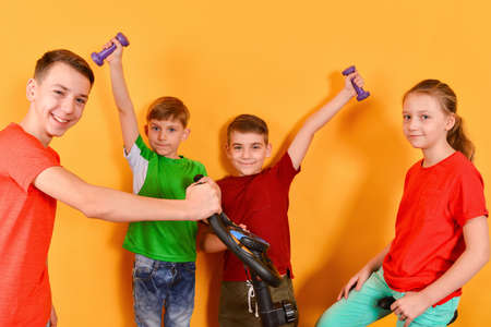 Girl sitting on an exercise bike, boys with dumbbells in their hands hold them to the sides on a yellow background, the concept of sport and healthy lifestyleの写真素材