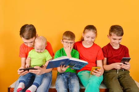 Children with a smartphone are sitting nearby, one boy in glasses is sitting with a bookの写真素材