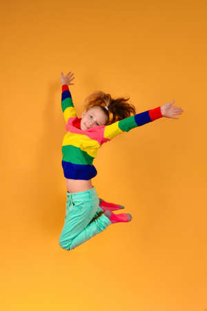 A girl in colored and bright clothes in a jump holds her hands to the sides and tightens her legs on...