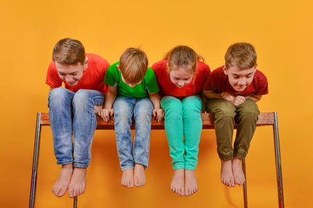 The four children are sitting barefoot, hanging their legs and leaning down looking downの写真素材