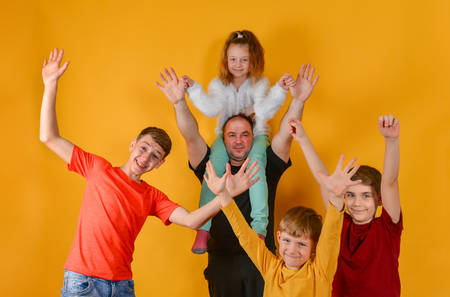 A father and four joyful children raised their hands up, a daughter sits on my fathers shoulders. Funny and funny beautiful children in colorful clothesの写真素材