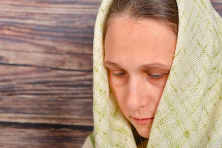 Young and beautiful grandmother in a woolen shawl looks down on a wooden background