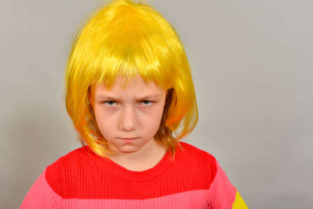 A girl in a yellow wig points to a place for an advertising product, a bright colored child on a gray backgroundの写真素材