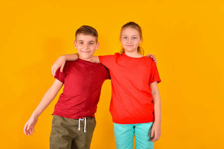 A boy with a girl in red t-shirts stand in an embrace on a yellow background. Joyful children, brother and sister.の写真素材