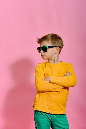 Beautiful fashionable and glamorous boy in sunglasses on a pink background