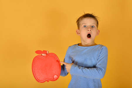 The boy holds in his hand a blank red plate in the form of an apple, a place for advertising or inscription.の写真素材