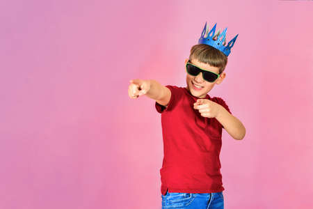 The boy in the blue crown on a pink background shows a finger forward.