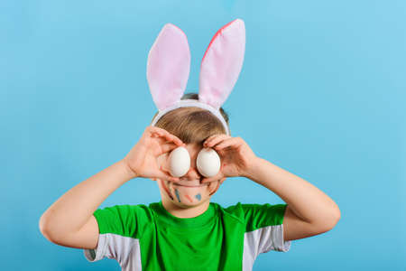 Boy with rabbit ears holds Easter eggs by the eyes, Easter holiday concept.の写真素材