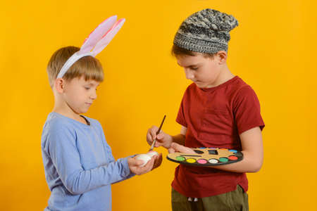 A young artist in a hat with a palette in his hand paints Easter eggs, the children are preparing...