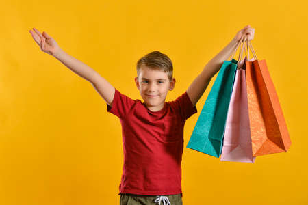 A joyful and happy buyer with colored bags in his hand shows his positive emotions from purchases. Baby with purchases on a yellow background.の写真素材