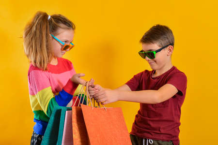 Boy and girl in sun glasses and with shopping bags, on a yellow background.