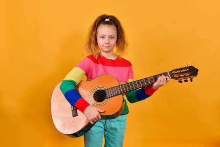 Girl with a guitar in a colored sweater, on a yellow background.