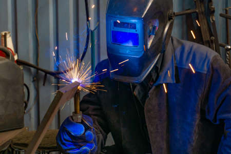A welder in a workshop manufactures and connects metal structures, a worker in a protective mask...