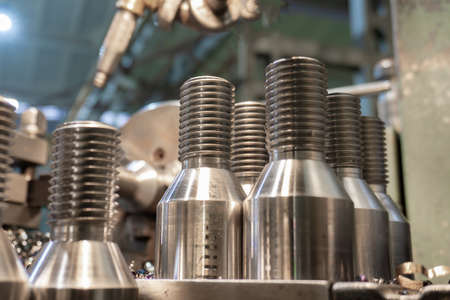 Bolt threading on a lathe in a machine shop, finished products on a machine bed.